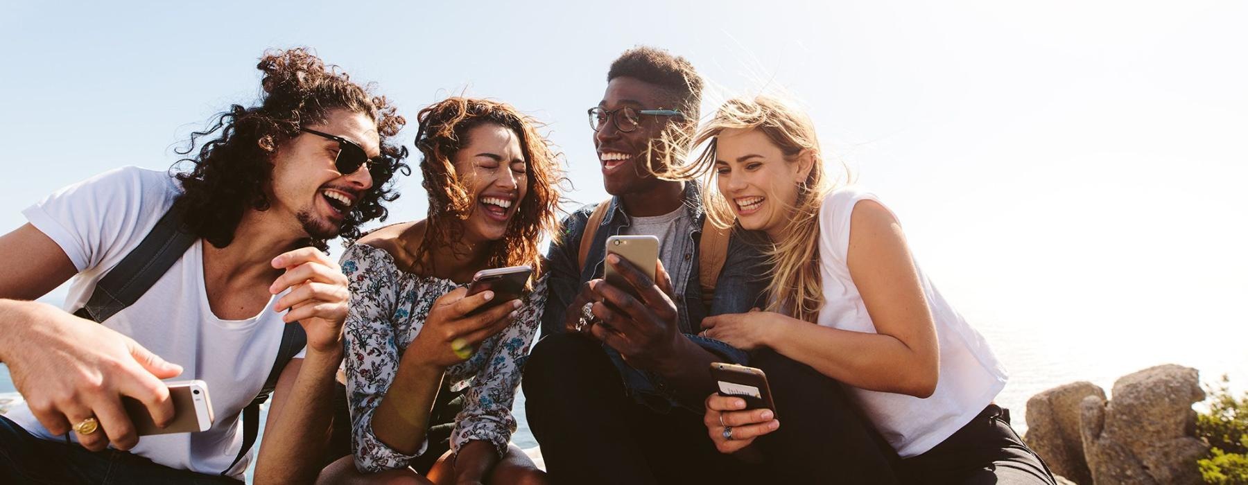 a group of friends sit outside laughing over their cell phones